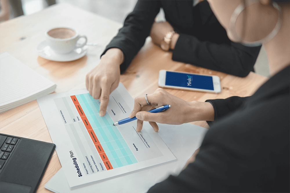 schedulingplan_mindsed two businesswomen with pen and iphone reviewing mindsed scheduling plan